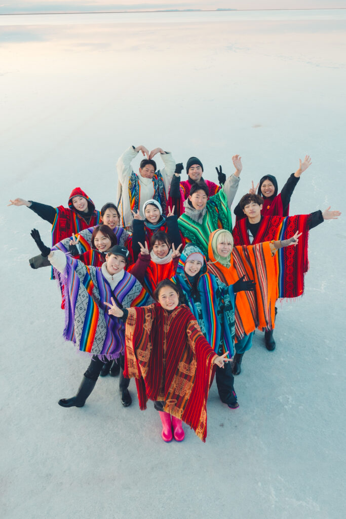 ウユニ塩湖の鏡張りに立つカラフルな民族衣装をした参加者たち旅人と広がる大空