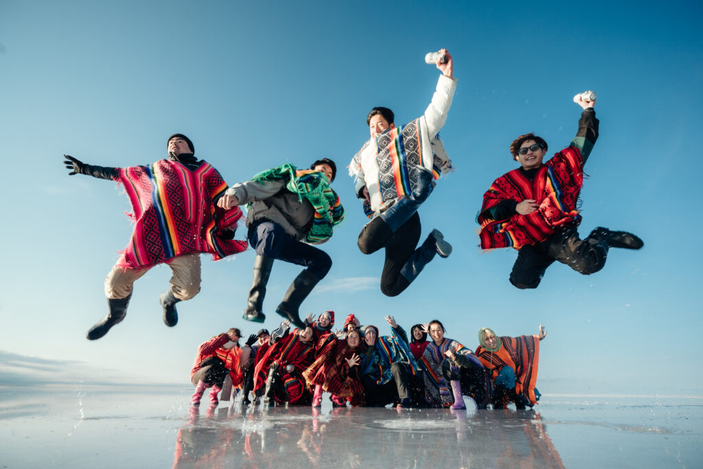 真っ青な鏡張りのウユニ塩湖で背景にジャンプする参加者たち